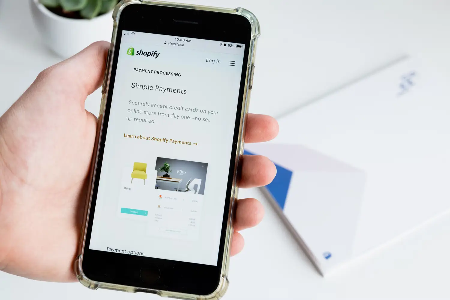 A hand holds a smartphone with Shopify store webpage open on it.